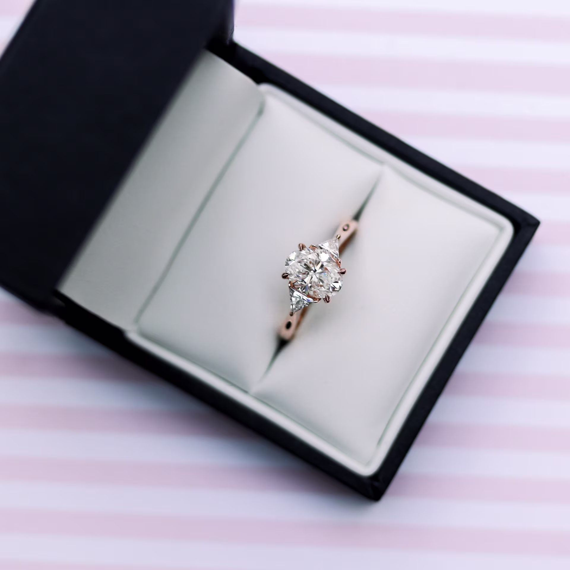 18k rose gold wedding ring with 2 ct oval laboratory grown diamond center stone accompanied by lab grown trillion side stones ada diamonds